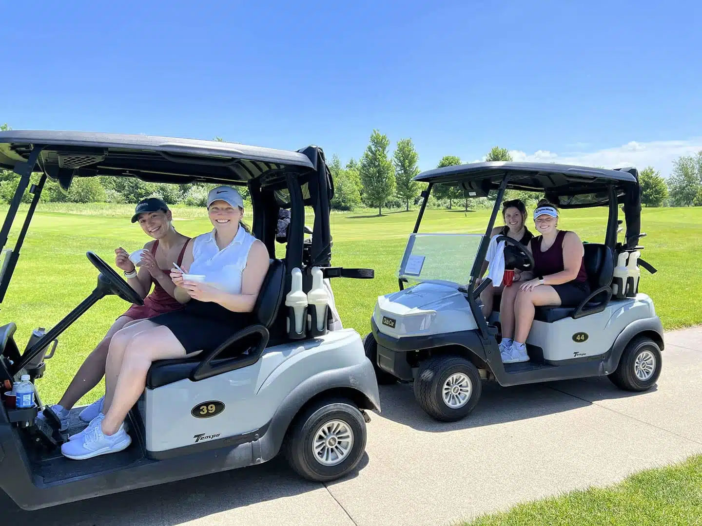 Four individuals riding on two golf carts